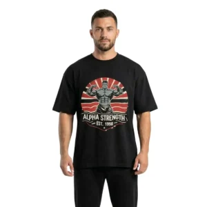 A frontal photograph of a fit male model wearing a premium black oversized gym t-shirt featuring a retro "Alpha Strength - Est. 1998" muscle graphic, on a white background.