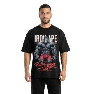 A frontal photograph of a muscular male model wearing a premium black oversized gym t-shirt featuring an intense "Iron Ape: Build Your Legend" gorilla lifting graphic, on a white background.